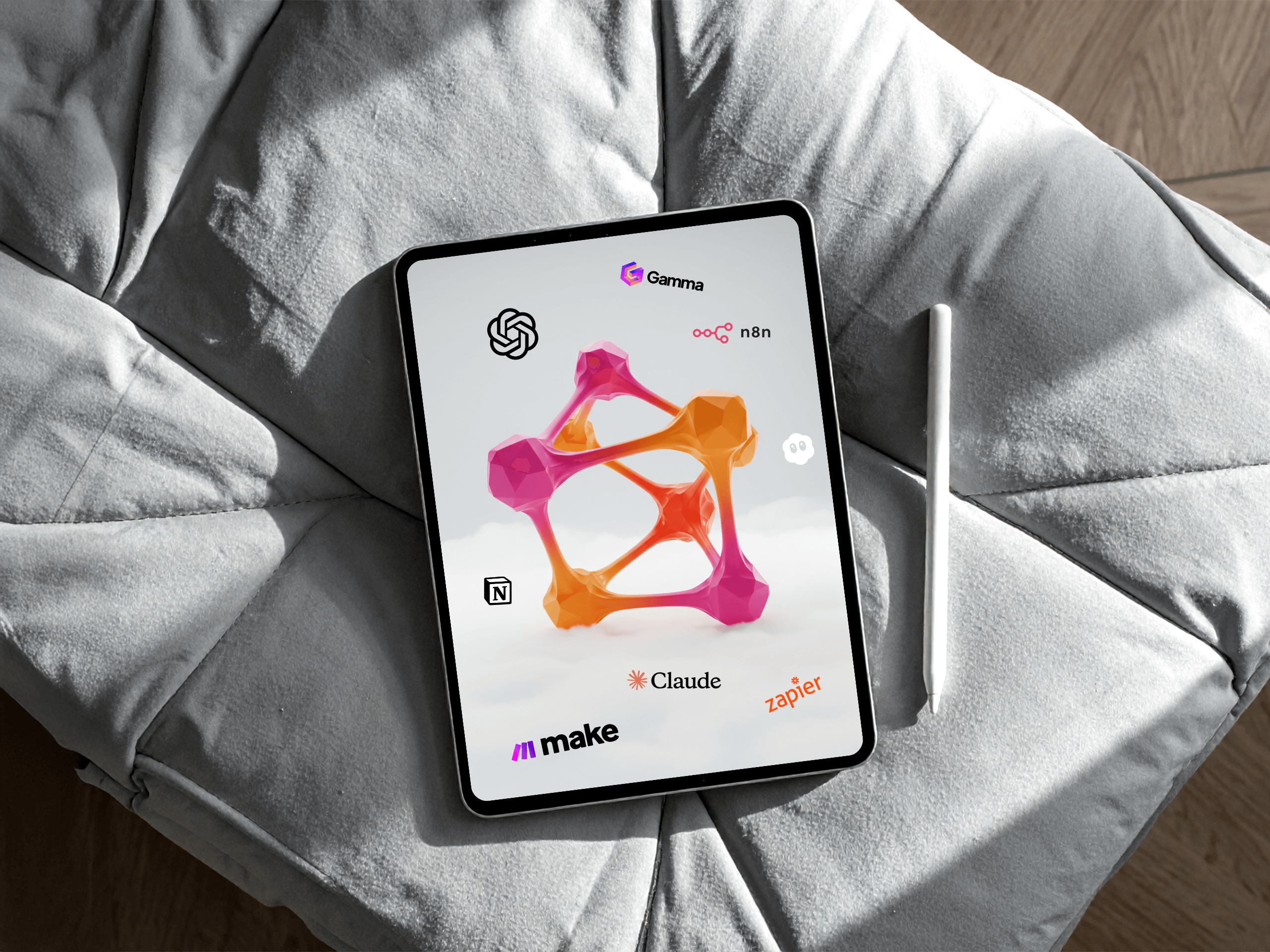Ein Tablet mit bunten 3D-Formen und Logos von Tech-Tools wie OpenAI, Gamma, Nat, n8n, Notion, Claude, Make und Zapier - die perfekte Inspiration für eine B2B-Agentur oder eine Unternehmenswebsite zum Thema KI und Automatisierung - liegt auf einem grauen, gepolsterten Stuhl mit einem Stift. - NINE brackets Digitalagentur München