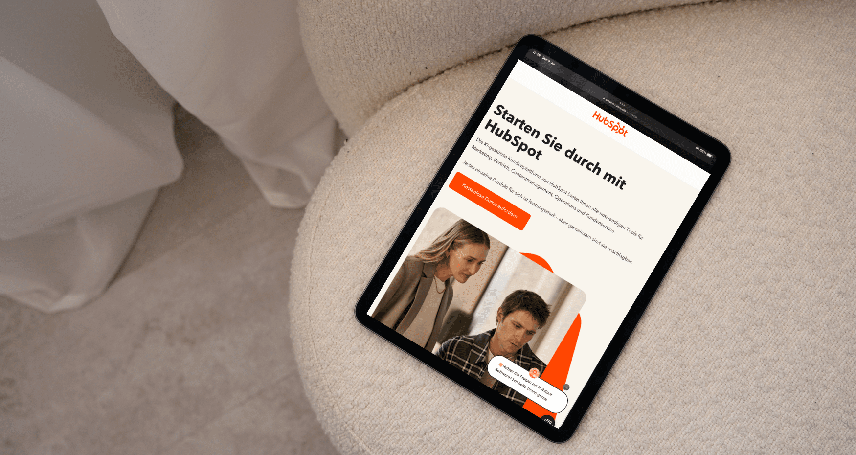 Ein Tablet auf einem beigen Stuhl zeigt eine deutschsprachige Unternehmenswebsite für eine B2B-Agentur mit einer Schlagzeile, einem orangefarbenen Button und einem Bild von zwei Personen, die zusammenarbeiten. - NINE brackets Digitalagentur München