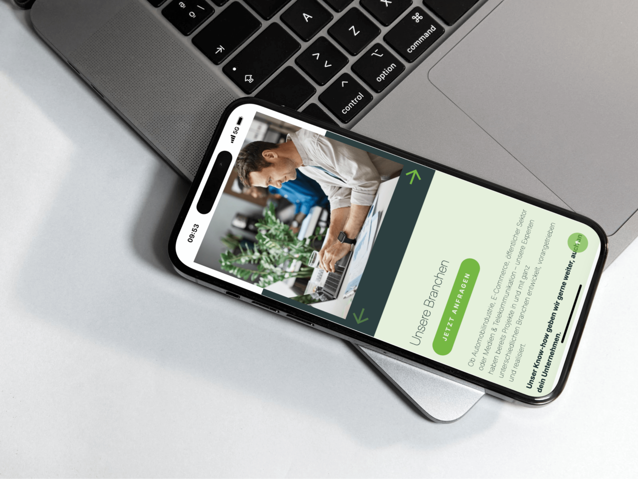Auf der Tastatur eines Laptops liegt ein Smartphone, auf dem die Unternehmenswebsite einer B2B-Agentur in deutscher Sprache angezeigt wird. Die Seite zeigt ein Foto von Menschen, die an Computern arbeiten, grüne Navigationstasten und Texte über KI und Automatisierung in verschiedenen Branchen. - NINE brackets Digitalagentur München