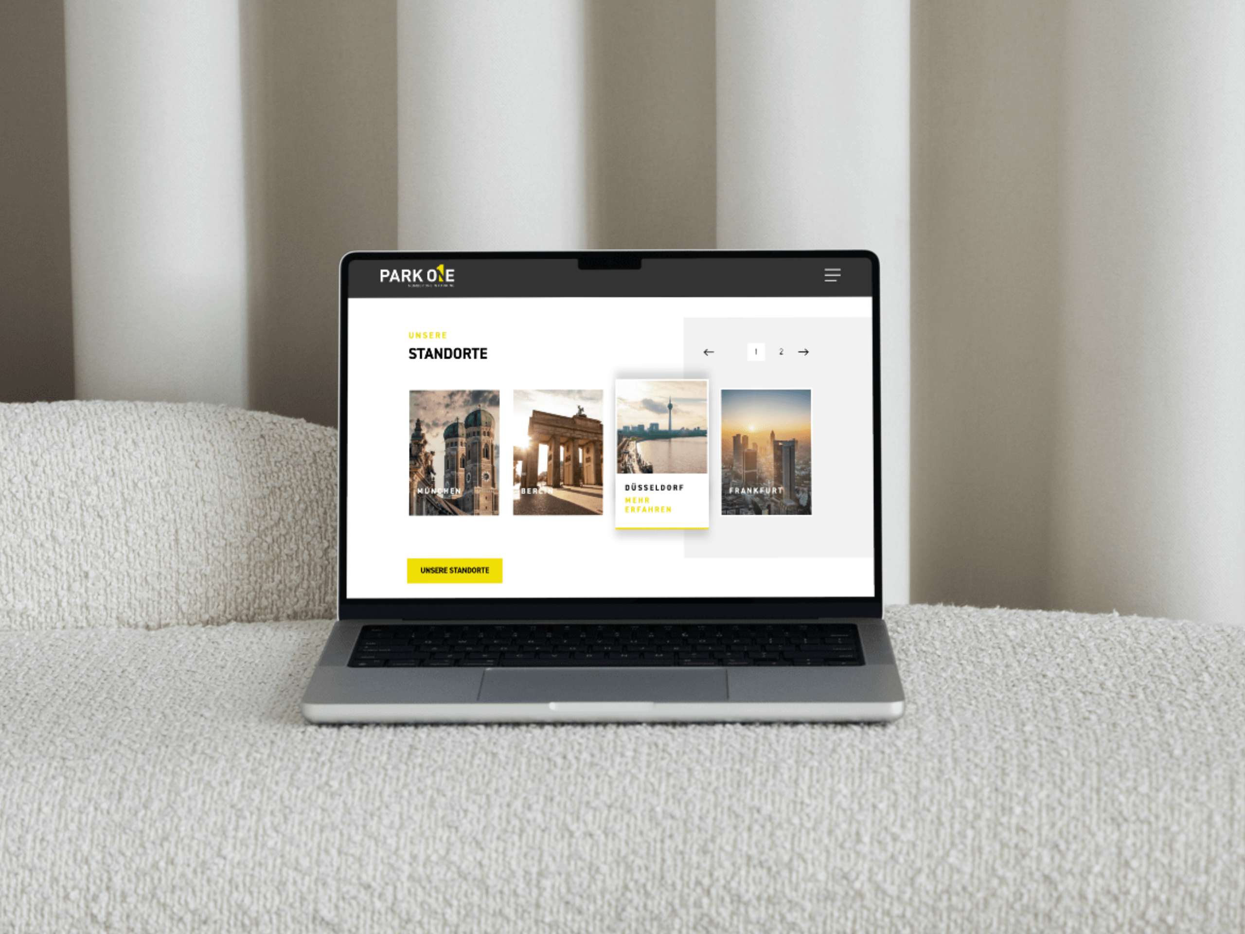 Ein Laptop auf einem hellen, strukturierten Sofa zeigt eine deutschsprachige Website mit Stadtansichten, dem fettgedruckten Wort STANDORTE und Inhalten zu ki und automatisierung. Im Hintergrund hängen neutrale Vorhänge. - NINE brackets Digitalagentur München